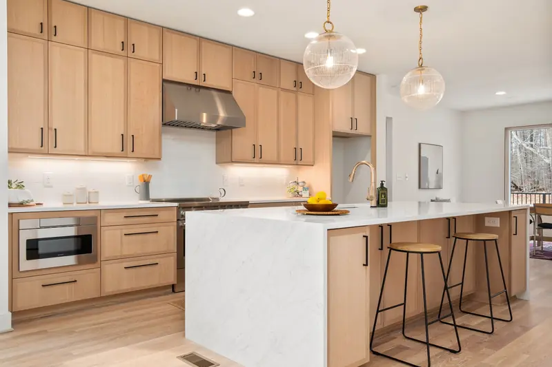 Built: a bright kitchen with pale oak cabinetry to the ceiling, a white stone waterfall island, two glass pendants and black stools.