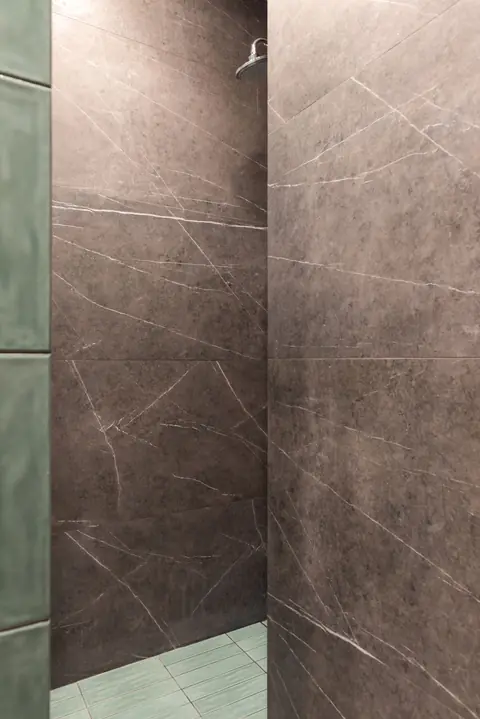 After: a walk-in shower lined in grey marble-look slabs with a band of green tile at the floor.