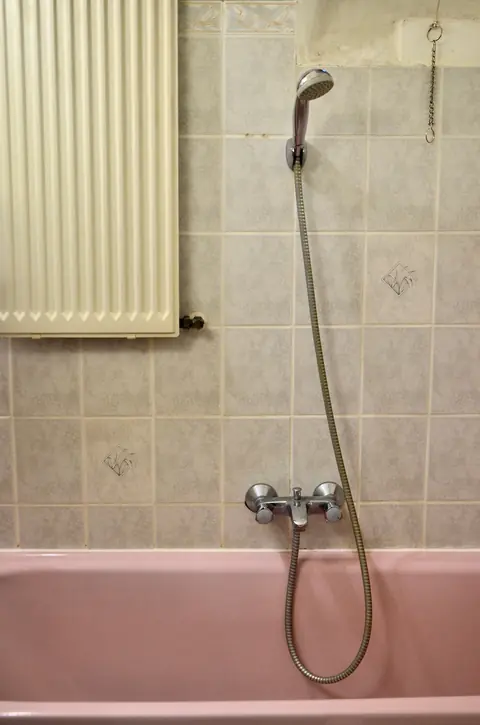 Before: a pink tub with a hand shower against beige patterned tile.