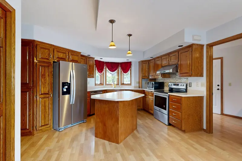 Before: a dated kitchen with orange oak cabinets, a red window valance and a small island on laminate flooring.