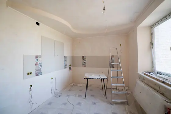 A kitchen stripped to fresh drywall with a ladder, a work table and protected floors.