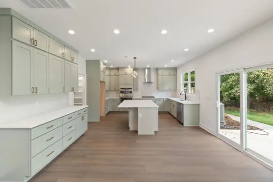 After: a long open kitchen with sage green shaker cabinets, a white island and sliding doors to a garden.