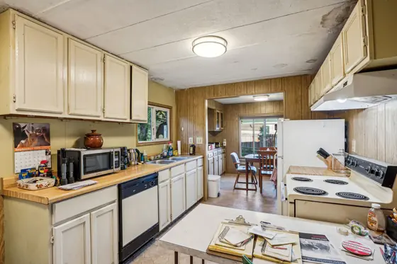 Before: a cramped kitchen with painted cream cabinets, wood paneling and a cluttered counter.