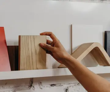 A hand drawing an oak sample from a shelf of terracotta and wood finish samples.