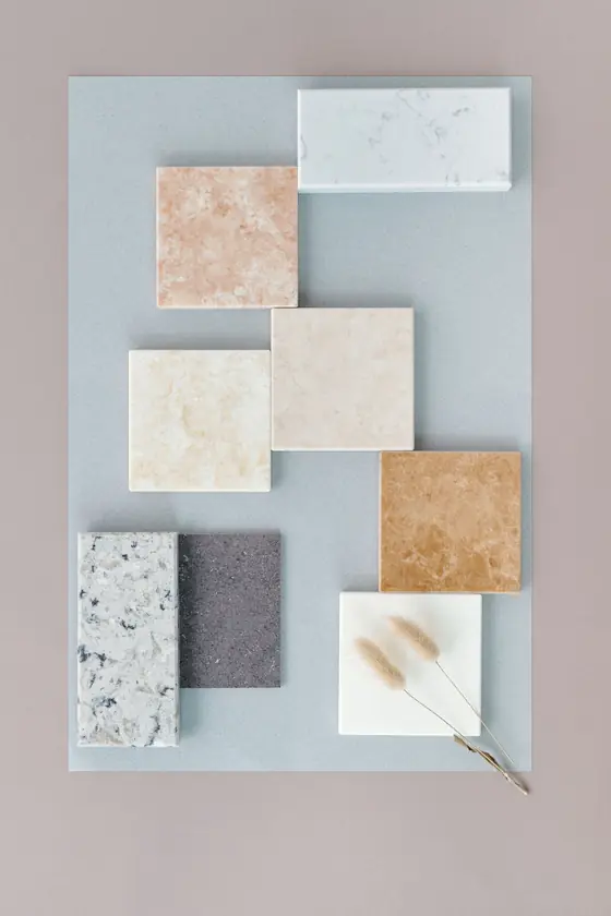 Stone and tile samples laid out on a pale table: terrazzo, travertine, rust-toned stone and white marble.